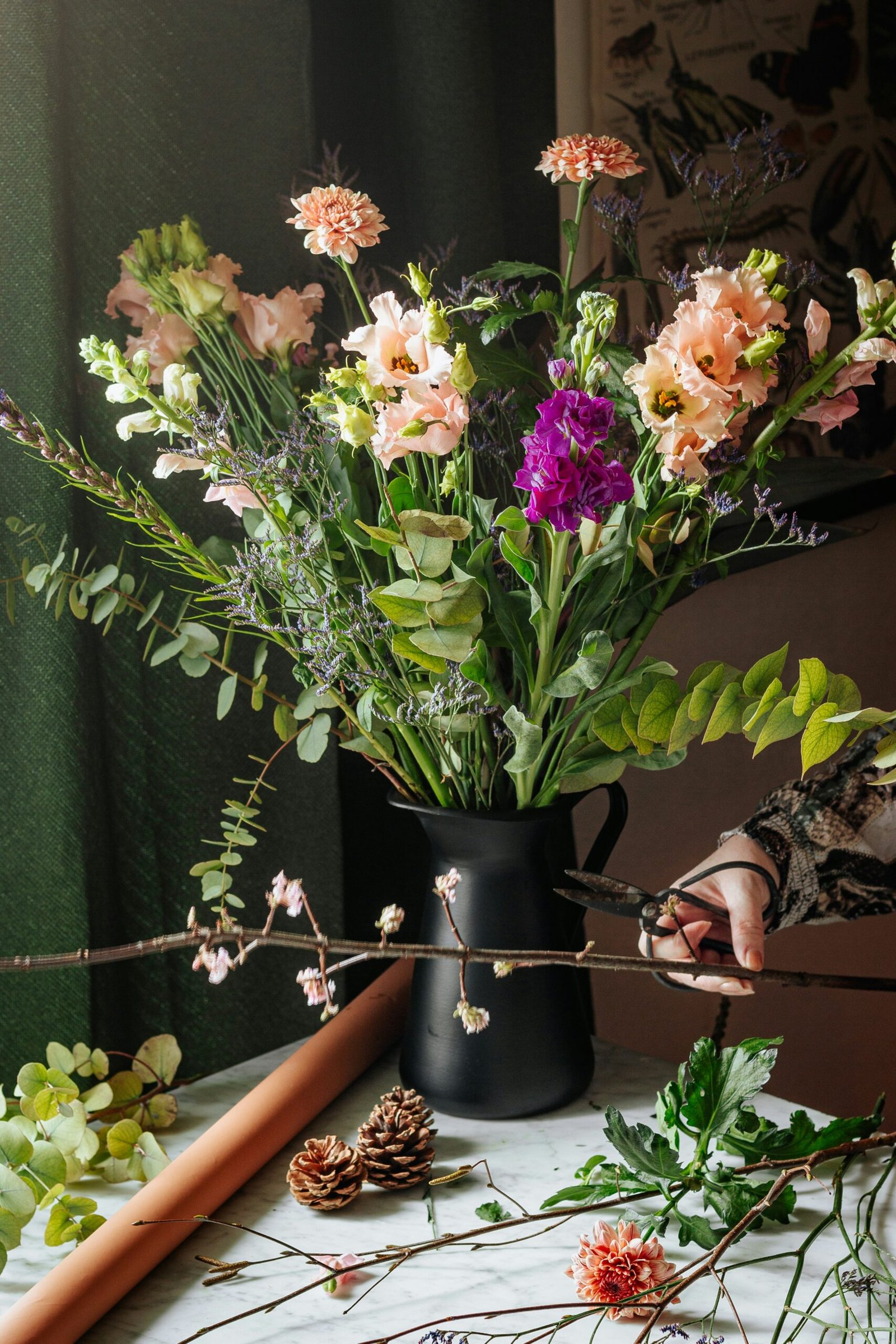 A woman's hand holding a pair of shears as she arranges a vase full of flowers.