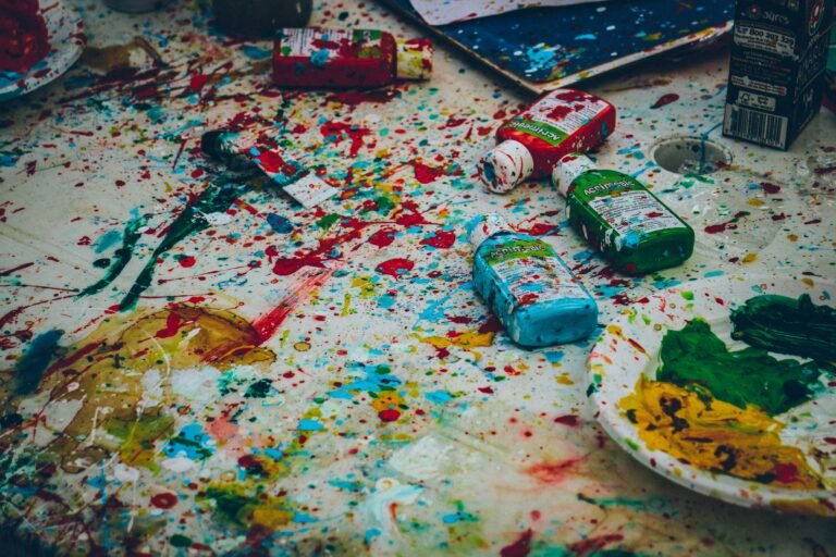 Bottles of paint scattered and spilled out over a table covered in a dropcloth.
